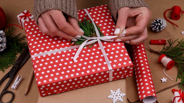 Close up woman hands packing and wrapping Christmas gift boxes with red paper, high angle view