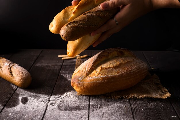 Close-up of woman hands take fresh bread. Dark photo