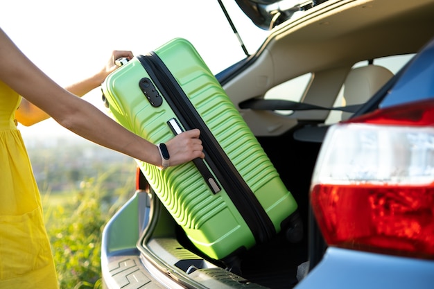 Close up of woman hands taking green suitcase from car trunk. Travel and vacations concept.