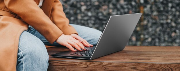 Close up of a woman hands typing in a laptop in the street against the background of an office build