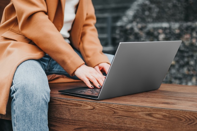 Close up of a woman hands typing in a laptop in the street against an office building. Businesswoman working distance. Close up