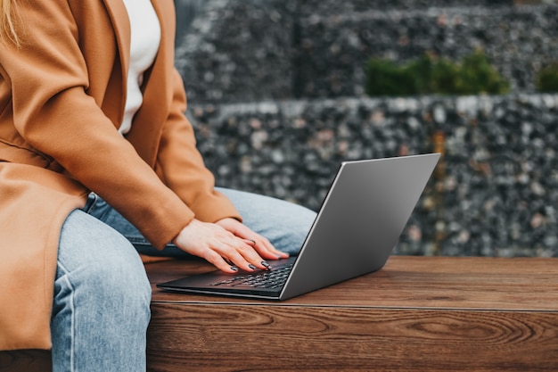 Close up of a woman hands typing in a laptop in the street against an office building. Businesswoman working distance