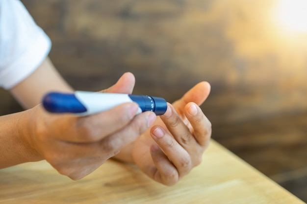 Photo close up of woman hands using lancet on finger to check blood sugar level