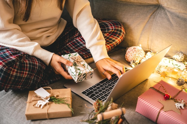 Close up of woman hands with gifts typing at laptop online shopping at christmas holidays cropped