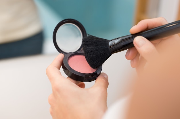 Close up of woman hands with makeup brush holding pink blush