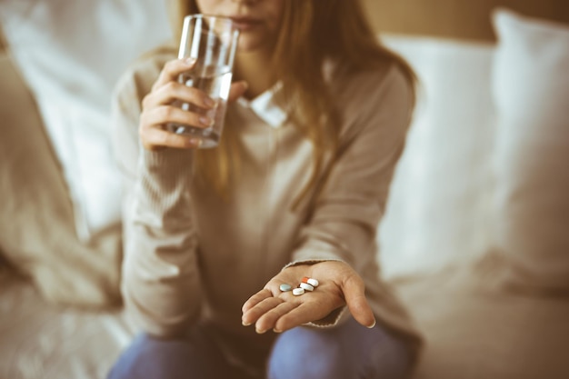 Close-up woman holding pills time to take medications, cure for headache, high blood pressure or cholesterol level remedy pain killer drugs. Stay at home concept during Coronavirus pandemic and self i