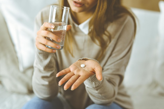 Close-up woman holding pills time to take medications, cure for headache, high blood pressure or cholesterol level remedy pain killer drugs. Stay at home concept during Coronavirus pandemic and self i