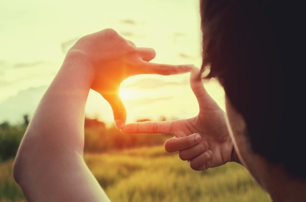 close up woman make hand framing gesture distant with sunset