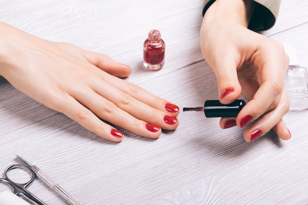 Close-up of a woman painting her nails with red lacquer