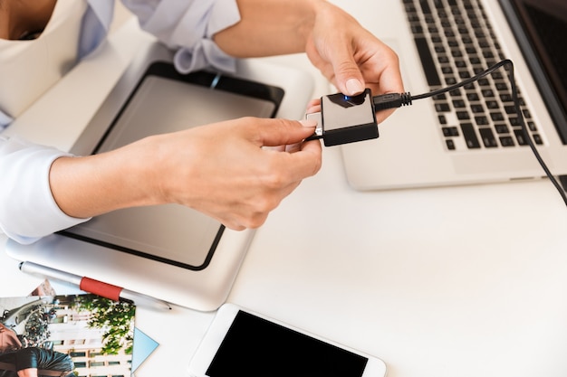 Close up of a woman photographer connecting hard disk drive to a laptop over table