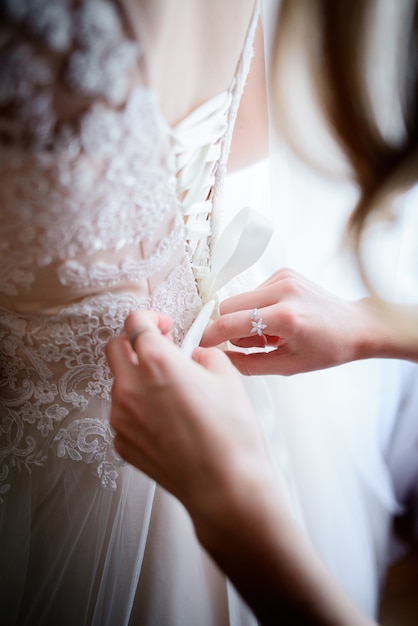 Close-up of woman's fingers lacing up bride's corset on her back