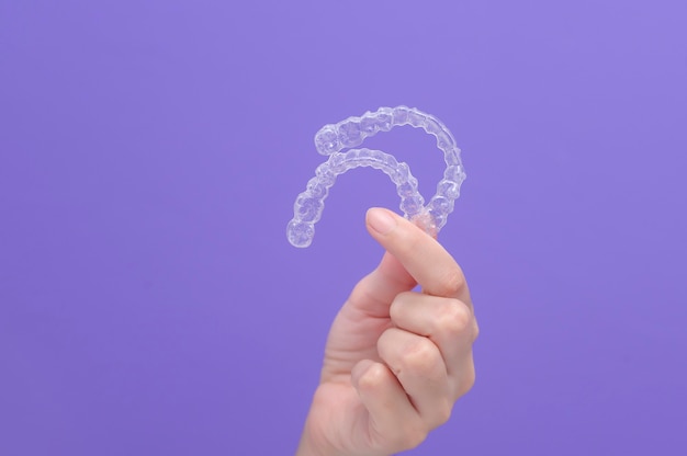 Close up of woman's hand holding invisalign braces in studio, dental healthcare and Orthodontic concept.