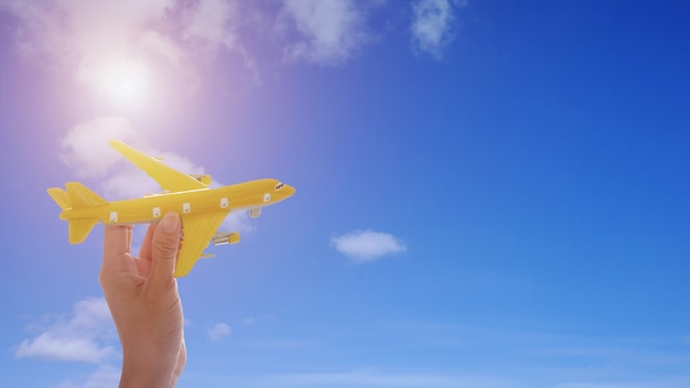 Close up of woman's hand holding toy airplane on blue sky background with sunshine.