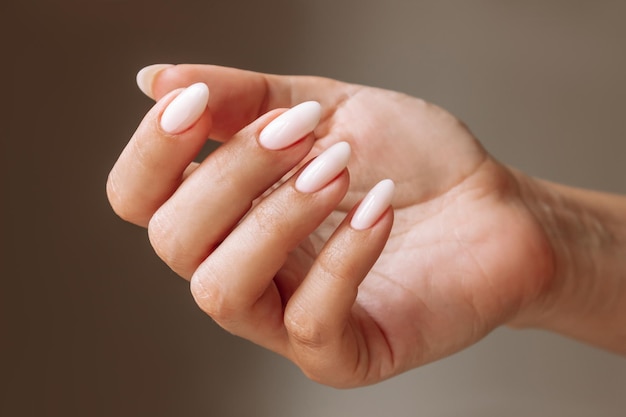 Close up of woman's hand with a perfect natural neutral delicate manicure on a dark brown background