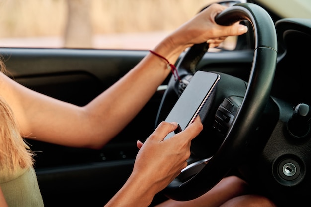 Close-up of a woman's hands driving while using her smart phone. Concept of traffic education and traffic accidents.