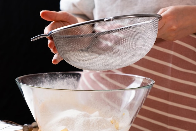 Close up woman sifts wheat flour through a sieve into mixing bowl for dough preparation for cake and