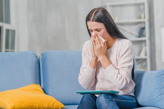 Close-up of woman sitting on blue sofa holding digital tablet on her lap suffering from cough