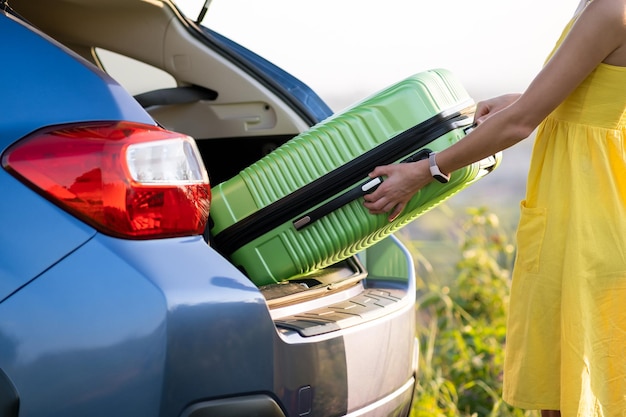 Close up of woman taking green suitcase from car trunk Travel and vacations concept