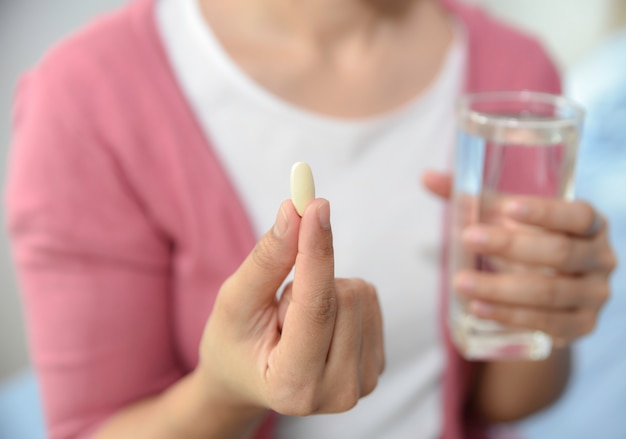 Close up of woman taking a vitamin C and holding a glass of fresh water at home. Diet, Nutrition, Healthcare, Medical supplements concept.