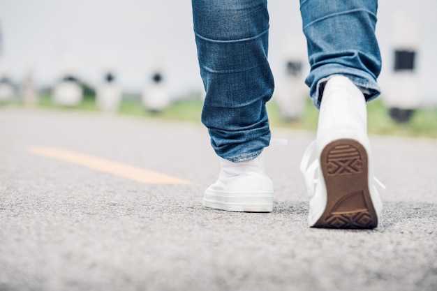 Close up woman wear jean and white sneaker walking forward on highway road