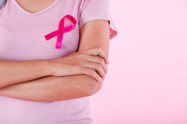 Close up of woman in with pink breast cancer awareness ribbon isolated on pink blank copy space studio background,healthcare,medicine concept