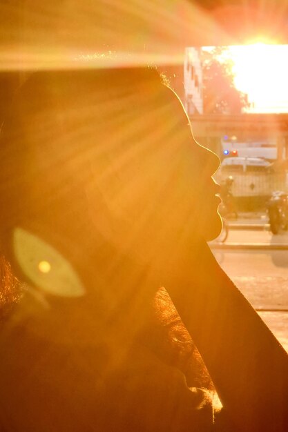 Photo close-up of woman with sunbeam against sky during sunset