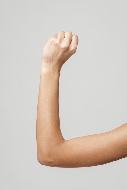 Photo close up of womans arm with fist raised in front of a grey background