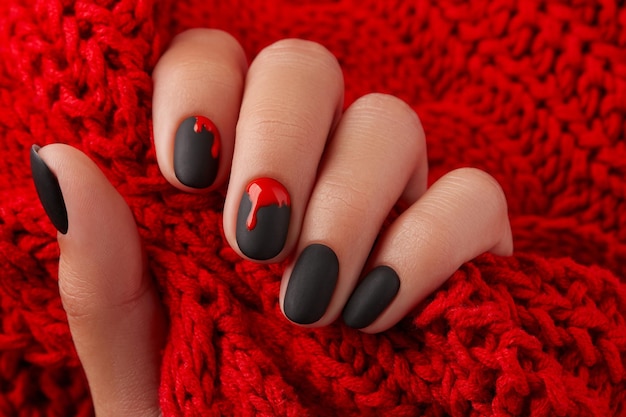 Close up womans hand with halloween manicure on red background holding fabric Manicure pedicure beauty salon concept