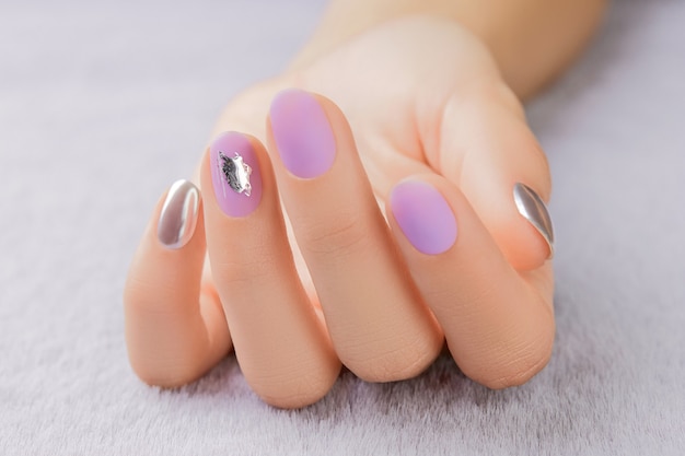 Close up womans hand with matte lavender nail design on gray furry background