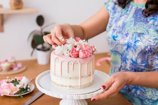 Close-up of women's hands decorating the cake with fresh flowers..