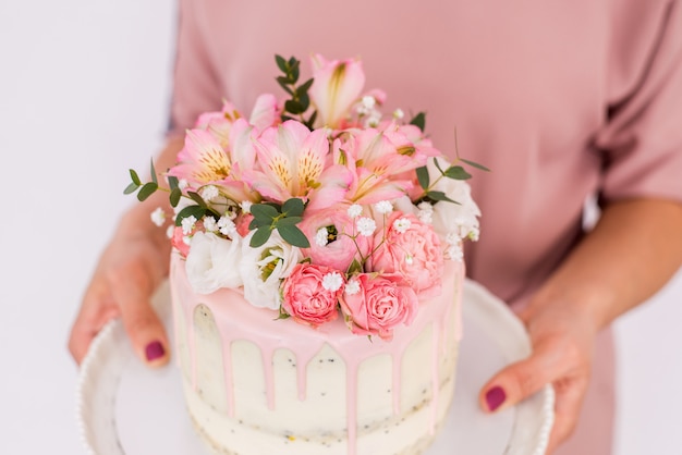 Close up of women's hands holding a cake decorated with flowers on a white background