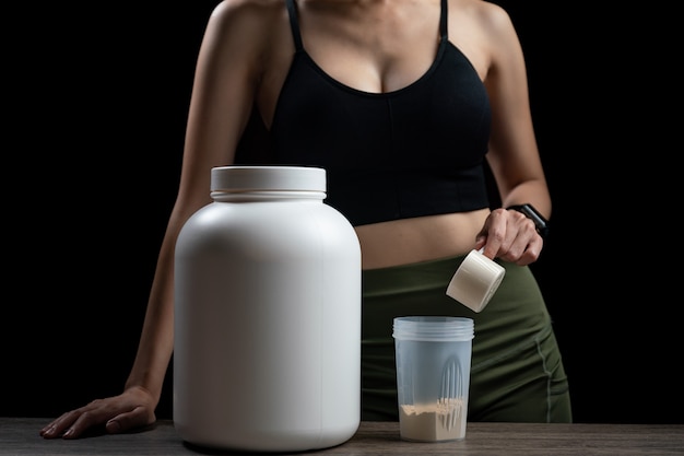 Photo close up of women with measuring scoop of whey protein, jar and shaker bottle, preparing protein shake.