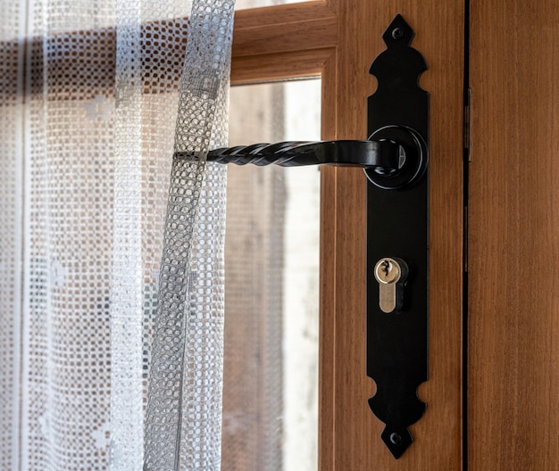 Close up of a wooden entrance door in brown color with a window, a curtain and a black handle.