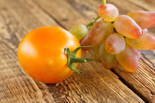 Close-up yellow tomato and bunch of grapes on wooden background. Shallow depth of field.