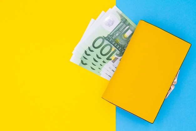 Close-up of yellow wallet with 100 Euro banknotes on a colored table