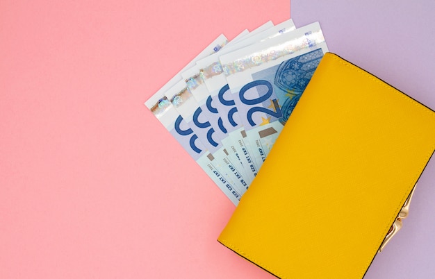 Photo close-up of yellow wallet with euro banknotes on a colored background