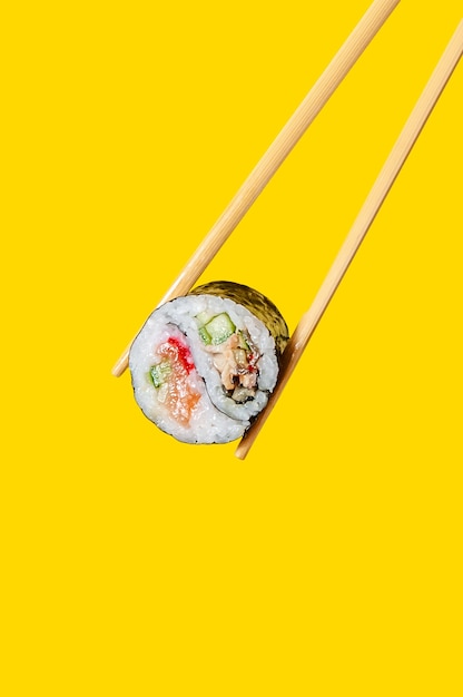 Close up Yin-Yang Roll with salmon fish, eel and cucumber on chopsticks on yellow background.