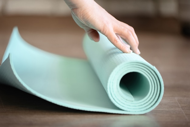 Close up yoga coach teacher preparing blue fitness mat for exercising in gym.