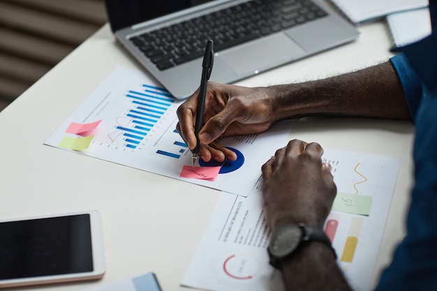 Close up of young africanamerican man working at desk in office and writing notes copy space