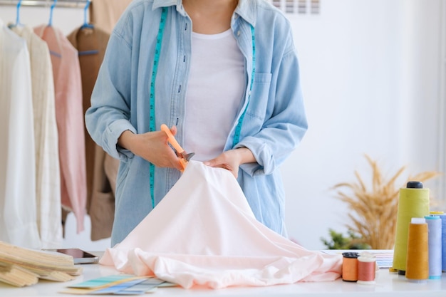 Close up of young asian female fashion designer is cutting fabric and prepare a pattern for a new