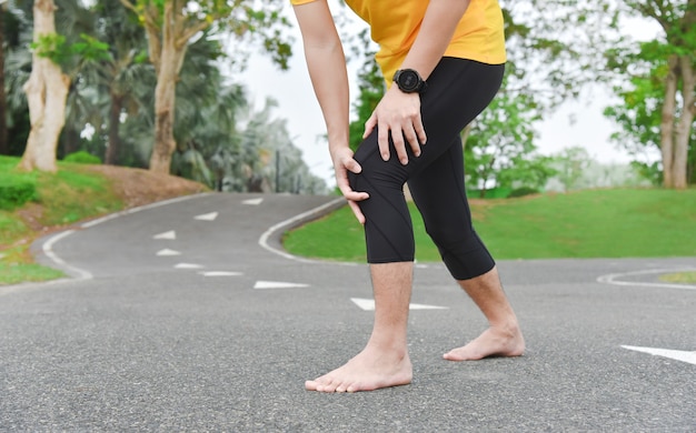 Close up of young Asian sports man has pain at muscles and joints during outdoor exercise, over trainning or running and sport injuty concept