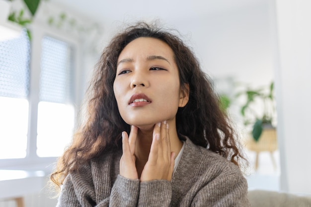 Close up of young Asian woman rubbing her inflamed tonsils tonsilitis problem cropped Woman with thyroid gland problem touching her neck girl has a sore throat