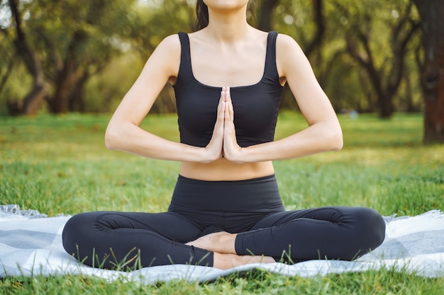 Close up of young attractive woman doing yoga in lotus position in the park.