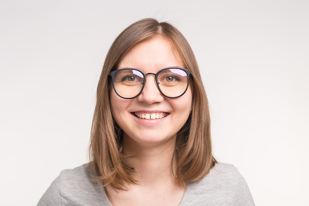 Close-up of young beautiful woman in glasses over white wall.