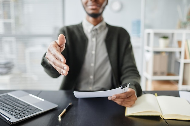 Close up of young black man holding out hand for greeting in job interview at office copy space