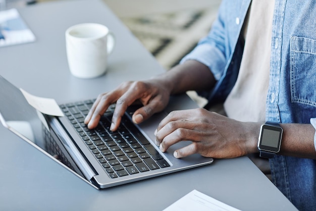 Close up of young black man typing at laptop keyboard while working remotely from home copy space