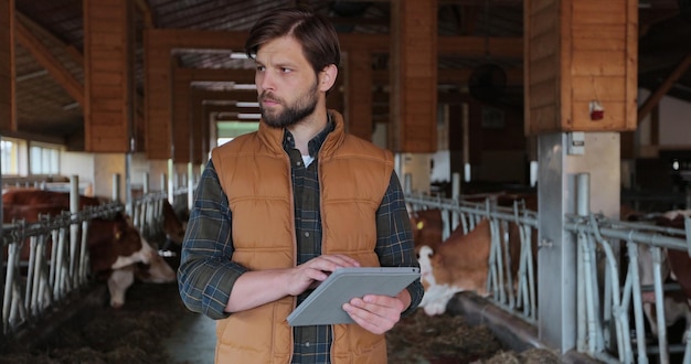 Close up young caucasian man in orange vest using tabletPC and working in farm Male farmer tapping and scrolling on tablePC in shed Farming concept