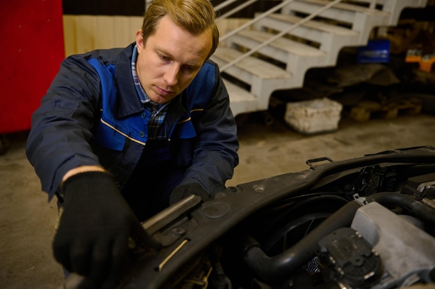 Close-up of a young Caucasian mechanic in car service adjusting headlights on car in the repair shop garage. Auto service, car repair and warranty maintenance concept