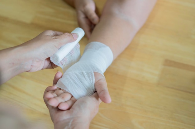 Close up of young female bandaging a white medicine bandage on old female hand