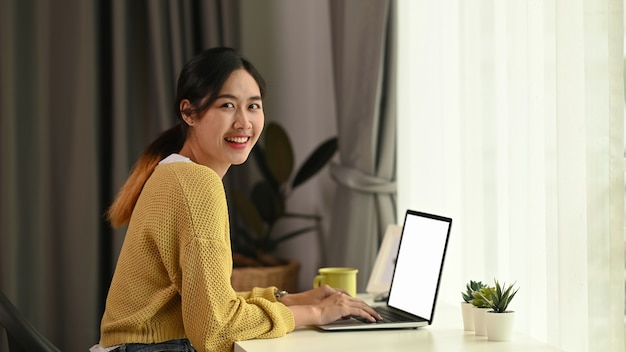 Close up of young female typing on laptop while sitting in front of blank screen laptop